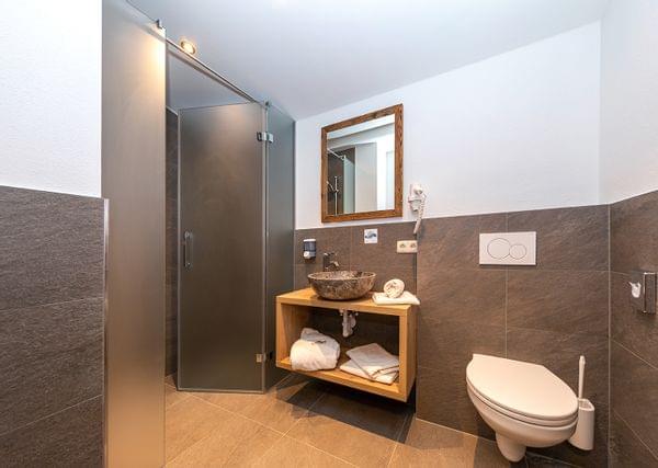 Modernes Hotelbad mit begehbarer Dusche, steinernem Waschbecken, Hängetoilette und Holzwaschtisch