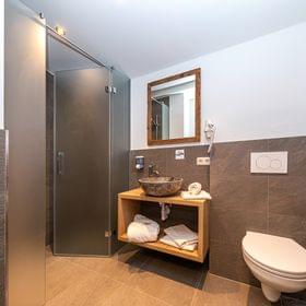 Modernes Hotelbad mit begehbarer Dusche, steinernem Waschbecken, Hängetoilette und Holzwaschtisch
