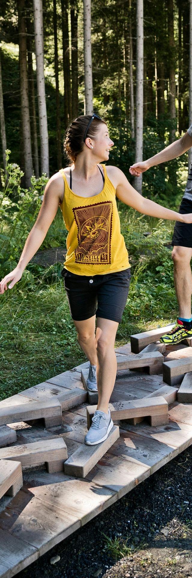 Couple balancing on wooden path in forest adventure trail on a sunny day