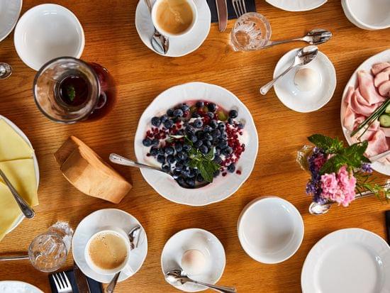 Frühstückstisch mit Joghurt, Beeren, Käse, Schinken, Eiern und Kaffee auf Holzoberfläche