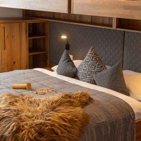 Gemütliches Hotelzimmer mit Holzmöbeln, Doppelbett, grauer Bettwäsche und Zierkissen