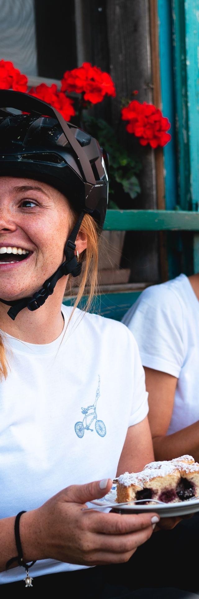 2 Frauen mit Radhelm auf bei Cafe und Kuchen vor einer Almhütte 