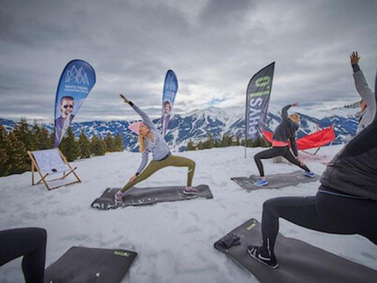 People doing outdoor yoga on snow-covered mountain with scenic alpine backdrop