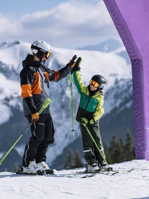 Erwachsener und Kind beim Skifahren geben sich High-Five auf der Piste in Saalbach vor Bergkulisse