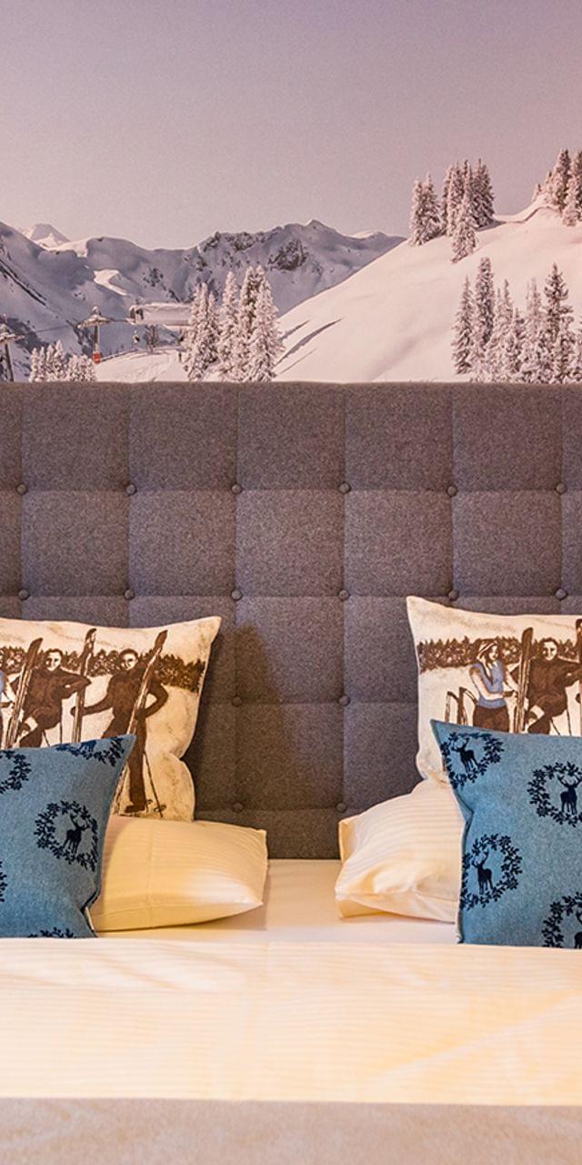 Gemütliches Doppelbett im Hotel mit Alpenkissen und Wandbild mit verschneiten Bergen