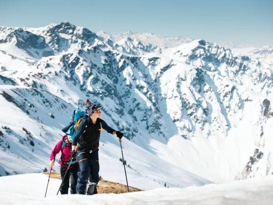Zwei Wanderer steigen mit Trekkingstöcken Schneehänge bei klarem Himmel hinauf