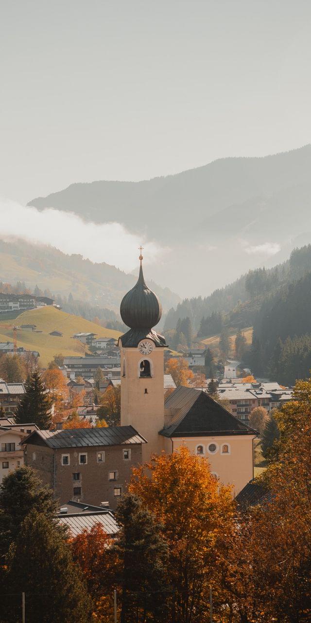 Alpendorf mit Kirchturm im herbstlichen Tal umgeben von bewaldeten Bergen