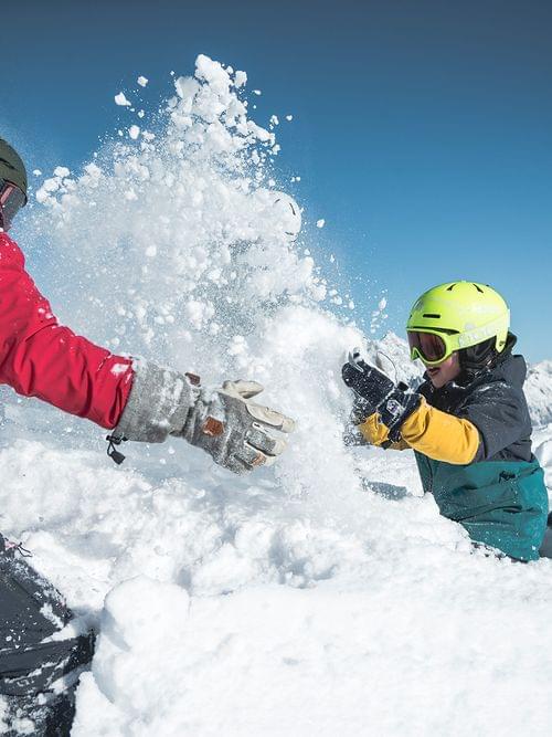 Two people playing in fresh mountain snow under blue sky in winter gear