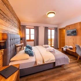 Cozy alpine hotel room with wooden walls, double bed, desk, and balcony access