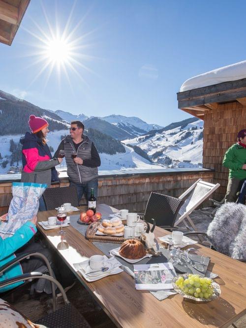 Group enjoying winter sun on chalet terrace with mountain view and breakfast