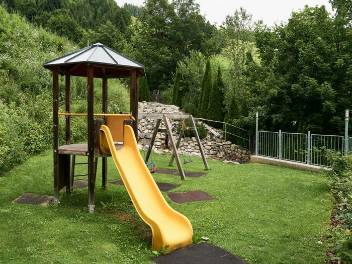 Yellow slide and wooden play structure in a grassy backyard playground