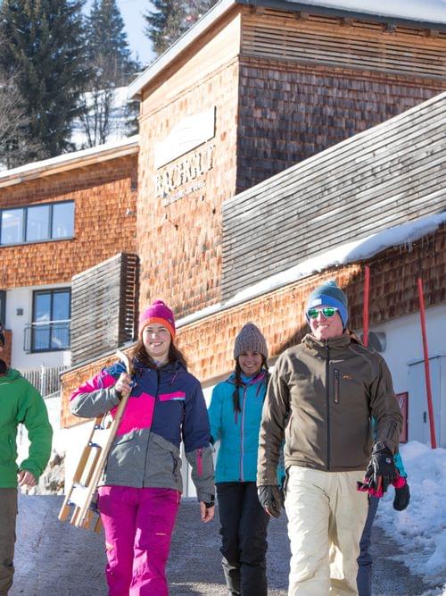 Group of people in winter gear carrying sleds near alpine lodge in snowy mountain resort
