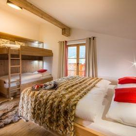 Cozy alpine hotel room with double bed, bunk beds, wood decor, and mountain view
