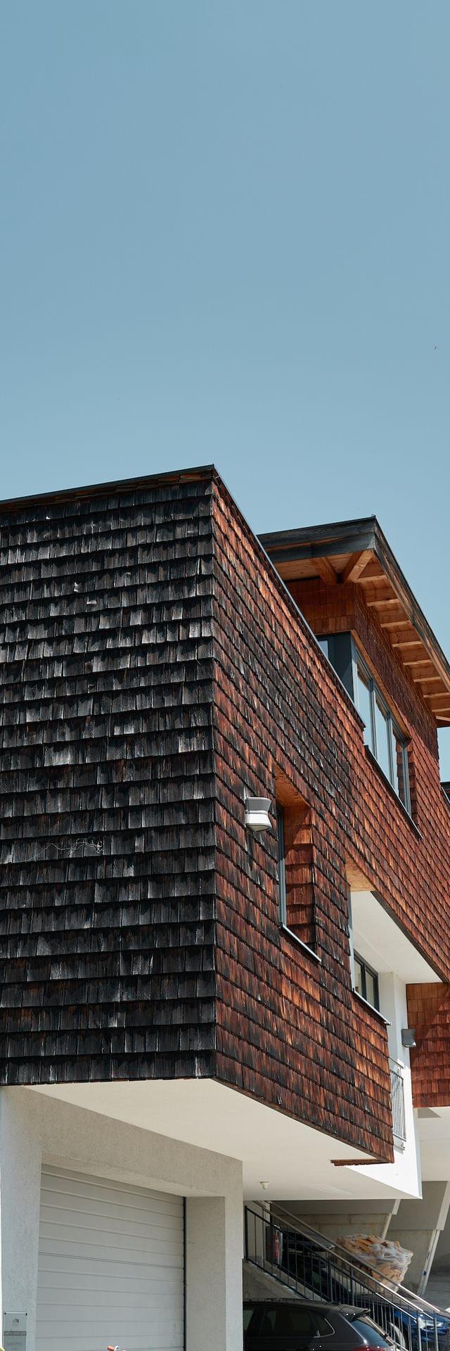 Chalets am Berg mit Holzfassade umgeben von Bäumen und Wiesen mit der Aufschrift Bachgut – Das Resort am Berg 
