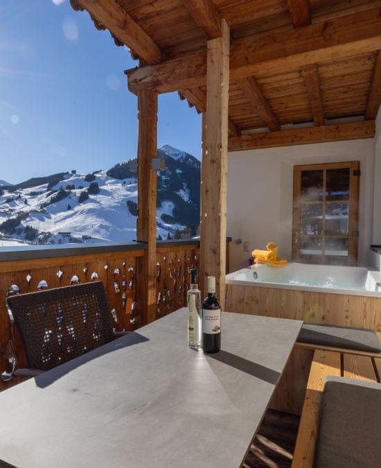Ausblick von der Terrasse der Stammhaus Suiten auf die Berge von Saalbach Hinterglemm im Winter, auf der Terrasse ist ein Whirlpool und eine gemütliche Stizgelegenheit zu sehen. 