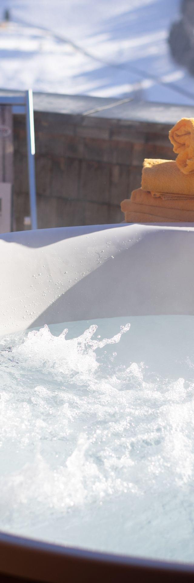 A bubbling hot tub on the terrace with lounge chairs, with a snowy winter landscape in the background.