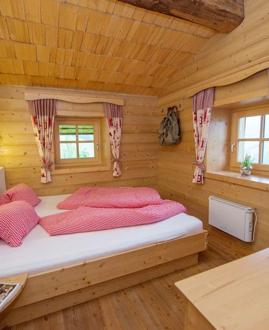 Cozy alpine bedroom with wooden walls, double bed in red checkered bedding, and rustic decor