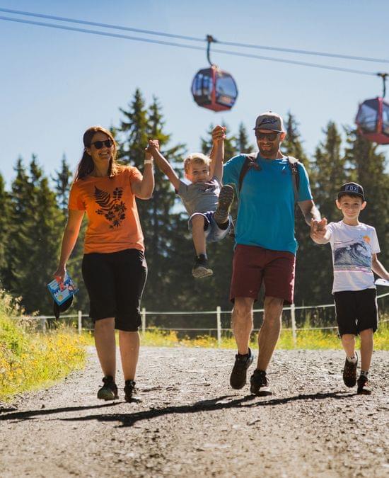Happy family hiking on a sunny mountain trail with gondolas in the background