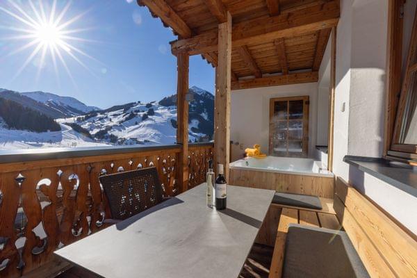 A view from the terrace of the main house suites overlooking the mountains of Saalbach Hinterglemm in winter, with a hot tub and a cozy seating area on the terrace.