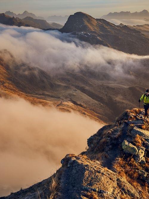 Wanderer mit Trekkingstöcken auf einem Bergrücken über nebligem Tal im Morgengrauen