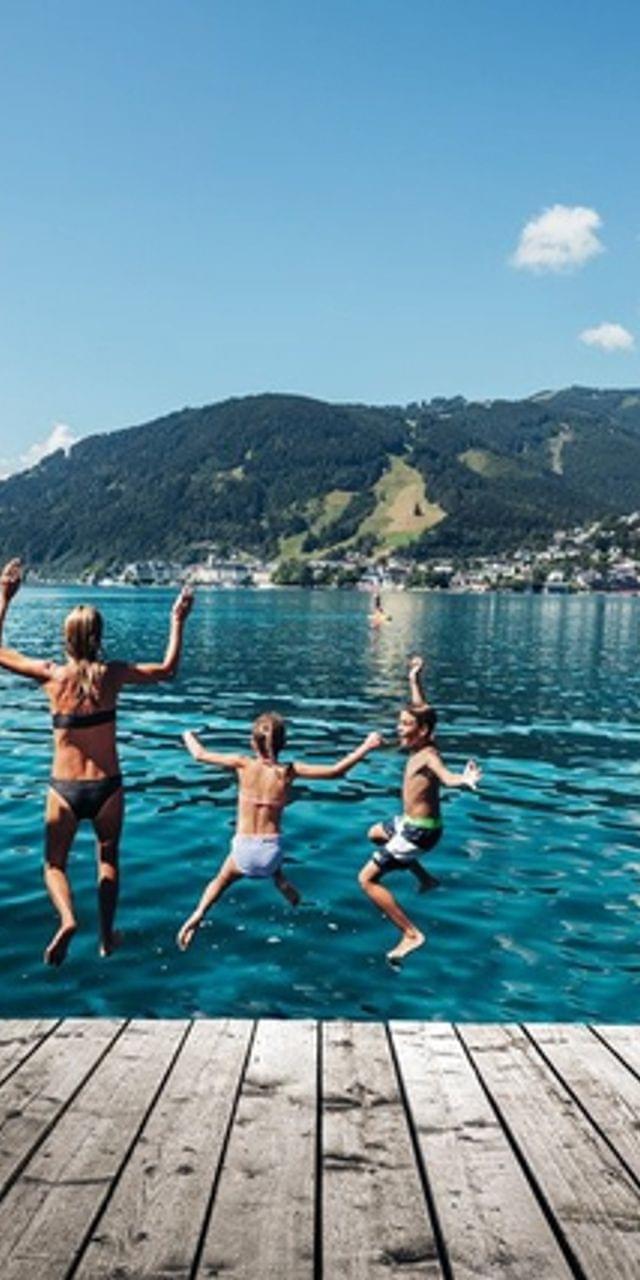 Gruppe springt im Sommer von Holzsteg in klaren Alpensee