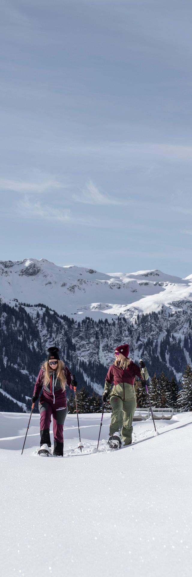 Zwei Frauen beim Schneeschuhwandern im Tiefschnee vor alpiner Bergkulisse