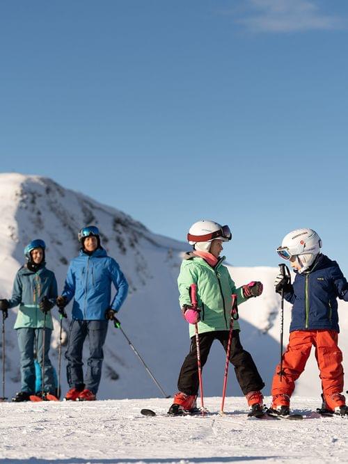 Family with two kids skiing on a snowy mountain slope under clear blue sky