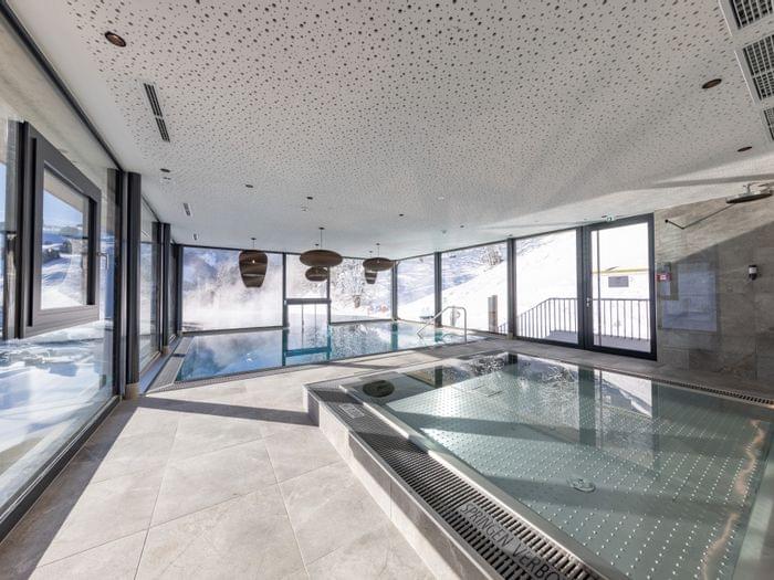 Bachgut Badehaus mit Kinder-Innenbecken und Schwimmbecken das nach draußen in den Invinity-Pool führt. Tief-Winterlich verschneite Landschaft im Hintergrund 