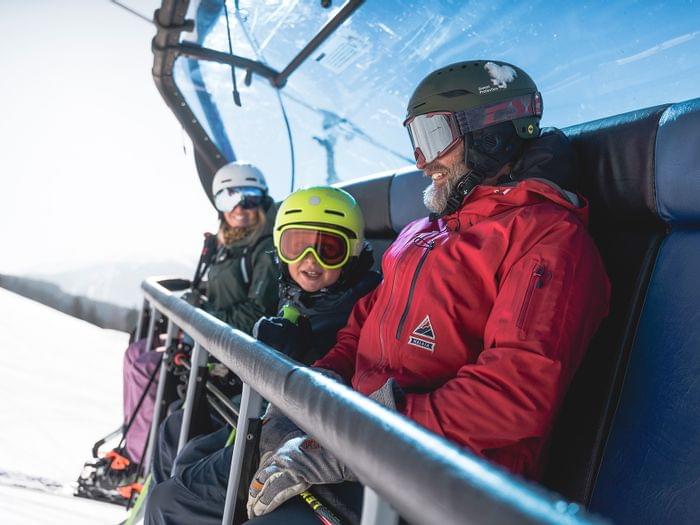 Family in ski gear riding ski lift on sunny day in mountain resort