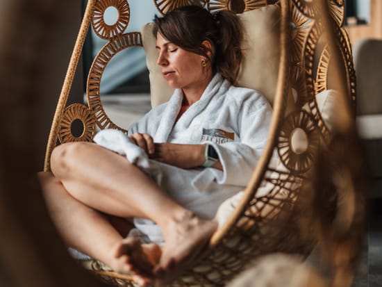 A woman in a bathrobe relaxing in a hanging chair.