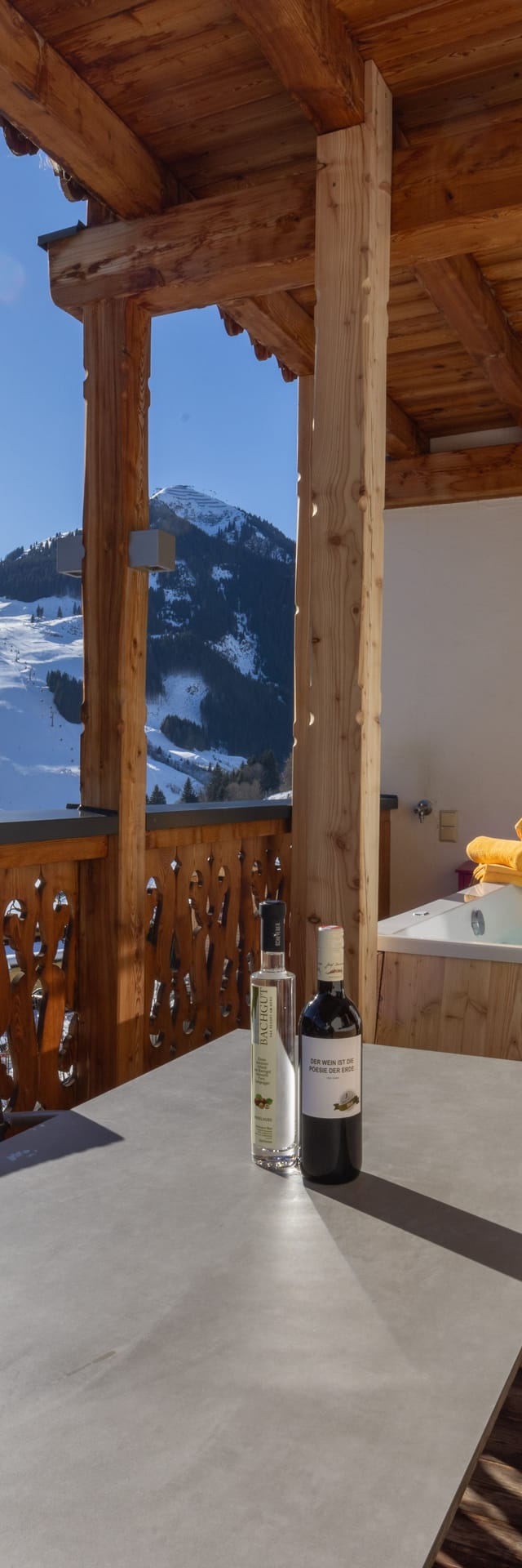 A view from the terrace of the main house suites overlooking the mountains of Saalbach Hinterglemm in winter, with a hot tub and a cozy seating area on the terrace.