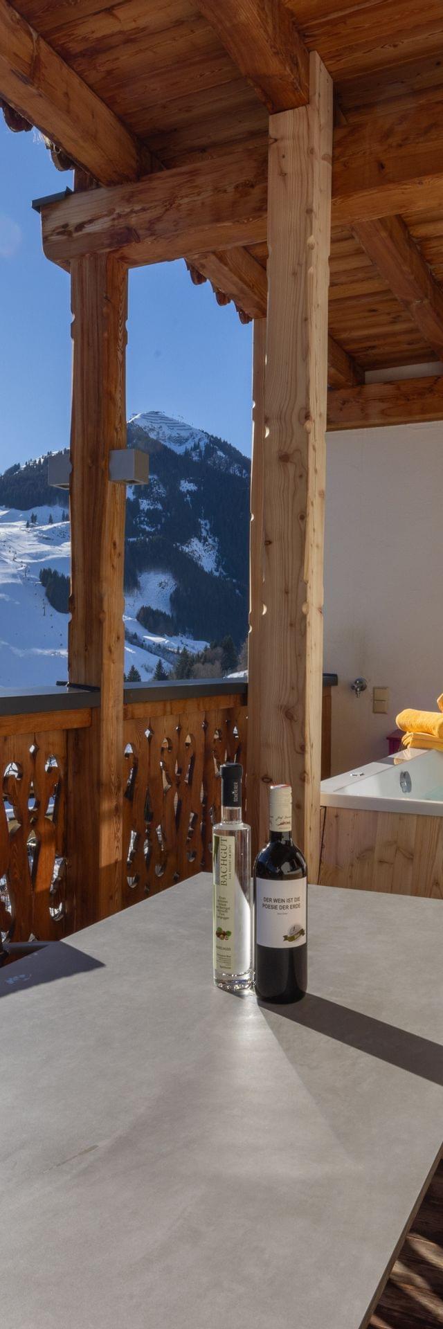 Ausblick von der Terrasse der Stammhaus Suiten auf die Berge von Saalbach Hinterglemm im Winter, auf der Terrasse ist ein Whirlpool und eine gemütliche Stizgelegenheit zu sehen. 