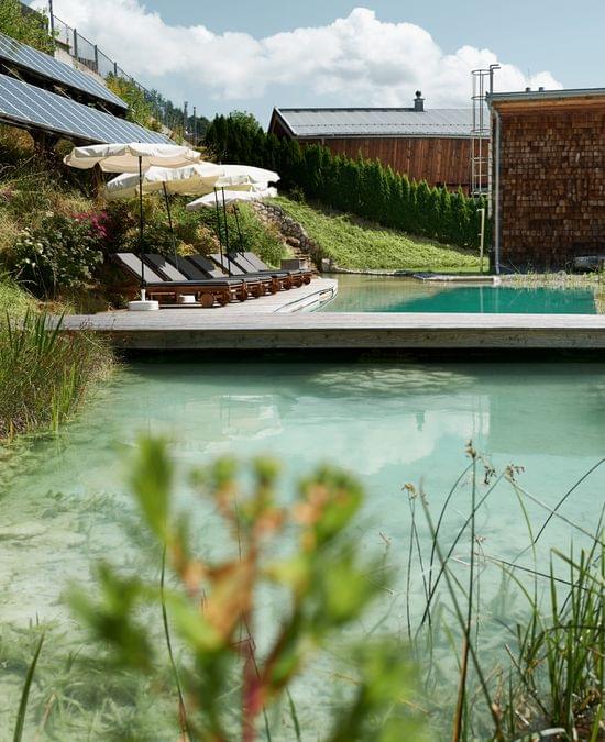 Ökohotel mit natürlichem Badeteich, Solarpanels, Liegen und Sonnenschirmen in grüner Hanglage