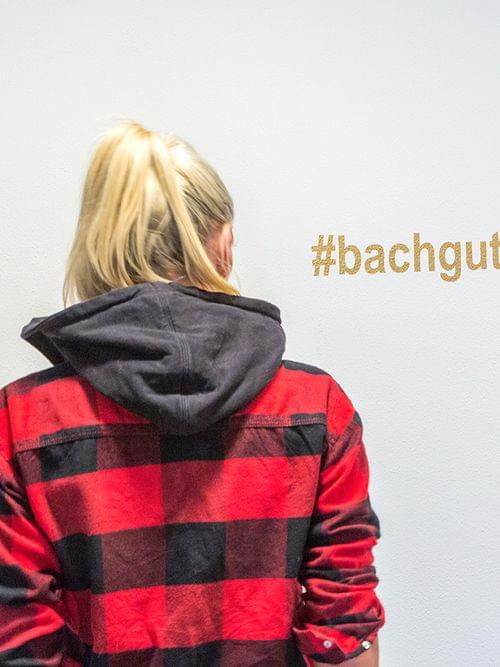 Woman in red plaid shirt facing wall with hashtag #bachgut