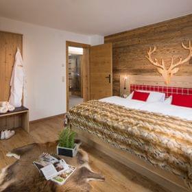 Gemütliches Alpenhotelzimmer mit Holzeinrichtung, Felldecke und roten Akzentkissen