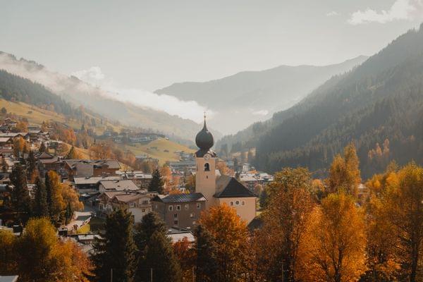 Alpendorf mit Kirchturm im herbstlichen Tal umgeben von bewaldeten Bergen