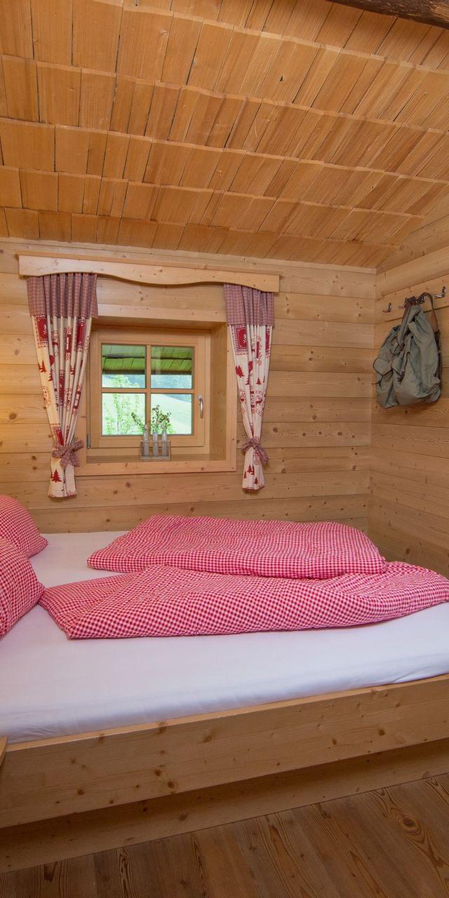 Gemütliches alpines Holzschlafzimmer mit rotkarierter Bettwäsche und traditionellen Vorhängen