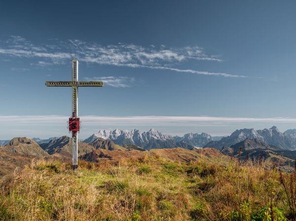 Gipfelkreuz auf Almwiese mit Panoramablick auf schneebedeckte Berggipfel