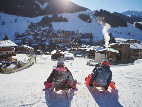 Rodelfahrer im Hintergrund verschneite Bergwelt und das Zentrum von Hinterglemm 