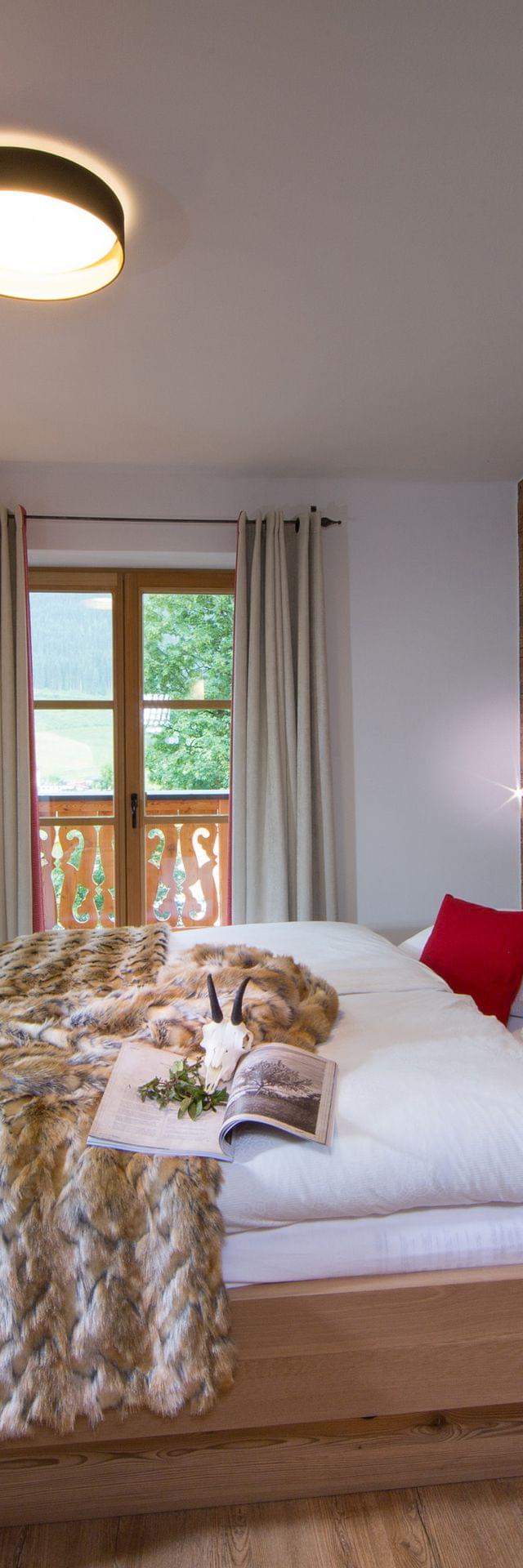 Gemütliches Alpenhotelzimmer mit Holzeinrichtung, roten Akzenten und Felldecke auf Doppelbett