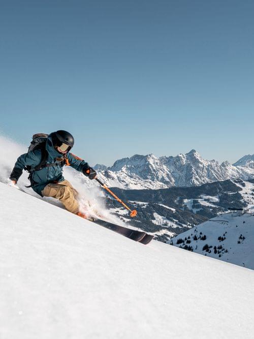 Skier carving down a snowy mountain slope with alpine peaks in the background