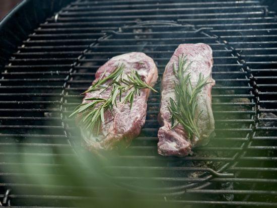 Rohe Steaks mit frischem Rosmarin auf einem Holzkohlegrill im Freien