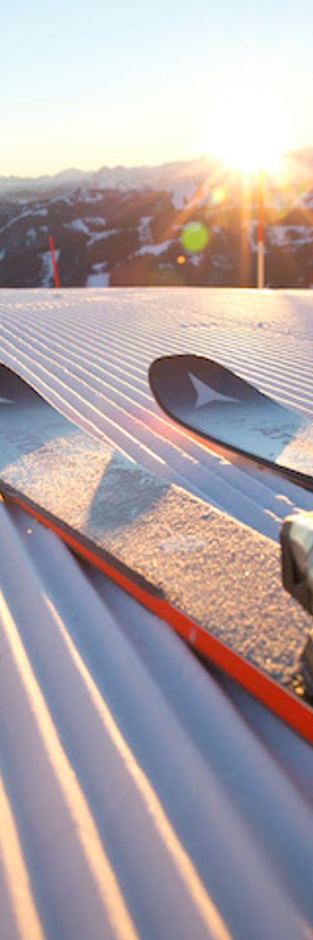 Skifahrer mit Skischuhen und Stöcken auf frisch präparierter Piste bei Sonnenaufgang