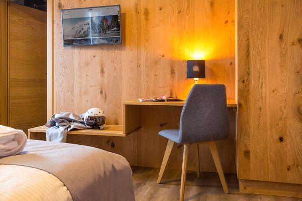 Gemütliches Hotelzimmer mit Holzwand, Flachbildfernseher, Skiausrüstung und Schreibtischlampe