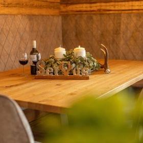Gemütlicher Holztisch mit Kerzen, Weingläsern und rustikaler Deko mit Schriftzug Servus