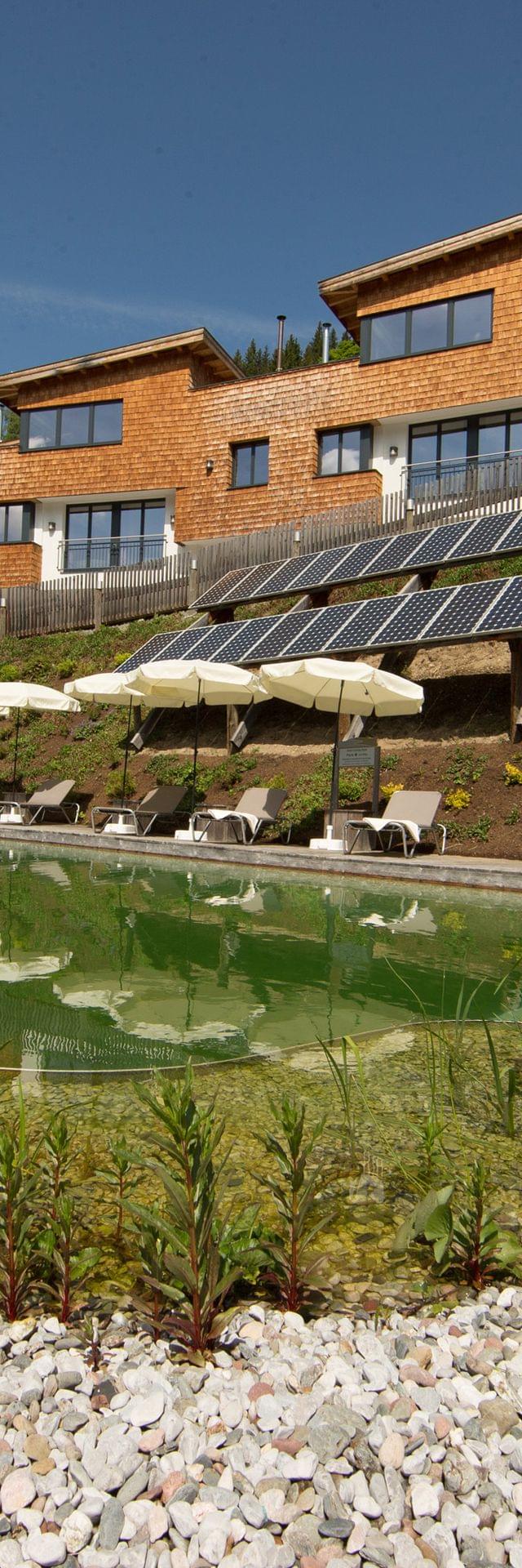 Eco-friendly resort with solar panels, natural swimming pond and wooden lodges on a hillside