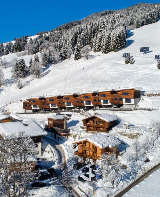 Schneebedecktes Alpendorf mit modernen Chalets und Skipisten an einem sonnigen Wintertag