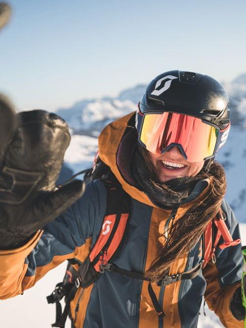 Smiling skier giving a high-five on a snowy mountain in bright winter sunlight