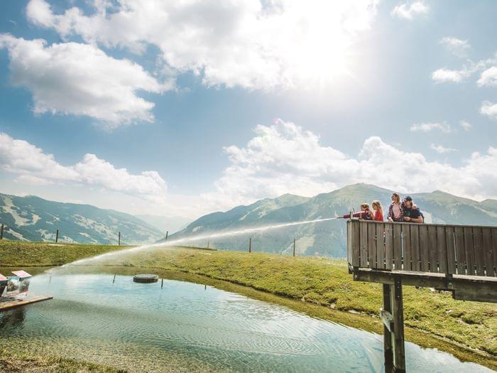 Family using water cannon at alpine fun park with scenic mountain view