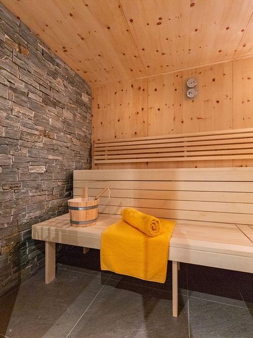 Moderne Holzsauna mit Steinwand, Bank, Ofen und zusammengerolltem gelben Handtuch